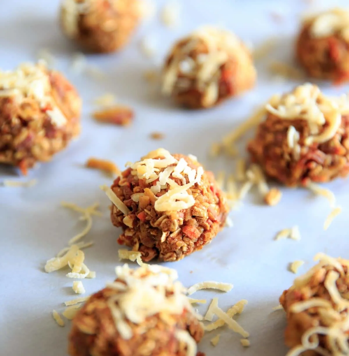 carrot cake energy bites on parchment paper, topping with shredded coconut flakes