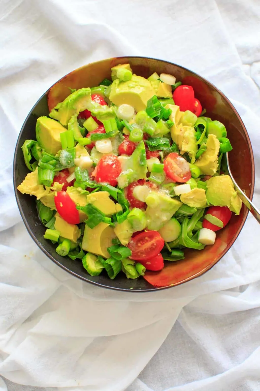 cucumber avocado salad with dressing with fork in brown bowl