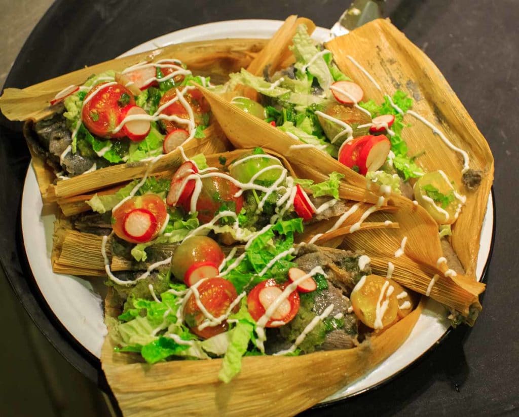 Peaceful River Farm Vegan Dinner by Fiction Kitchen - blue corn masa tamales with mixed kale, onions, oyster mushrooms finished with salsa verde, cilantro marinated cherry tomatoes, Chinese cabbage, radishes and crema