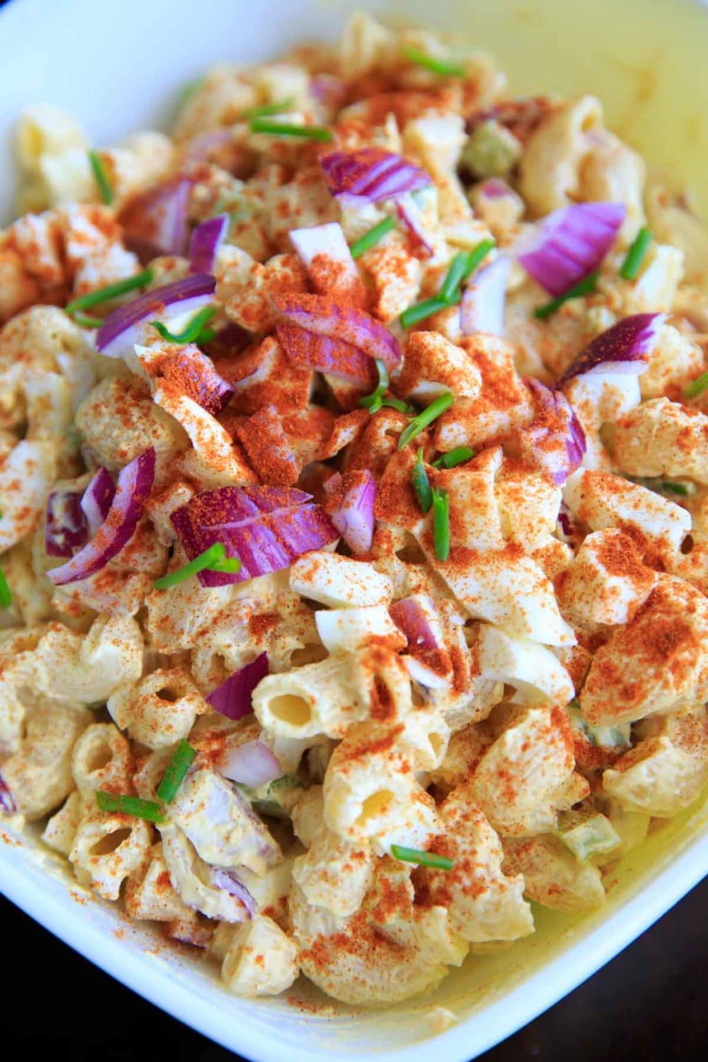 close up Deviled Egg Pasta Salad with macaroni and lots of red onions and paprika.