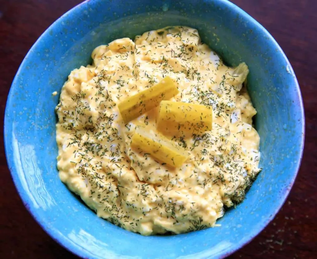 blue bowl of dill pickle egg salad with extra dill and pickle chunks sprinkled on top