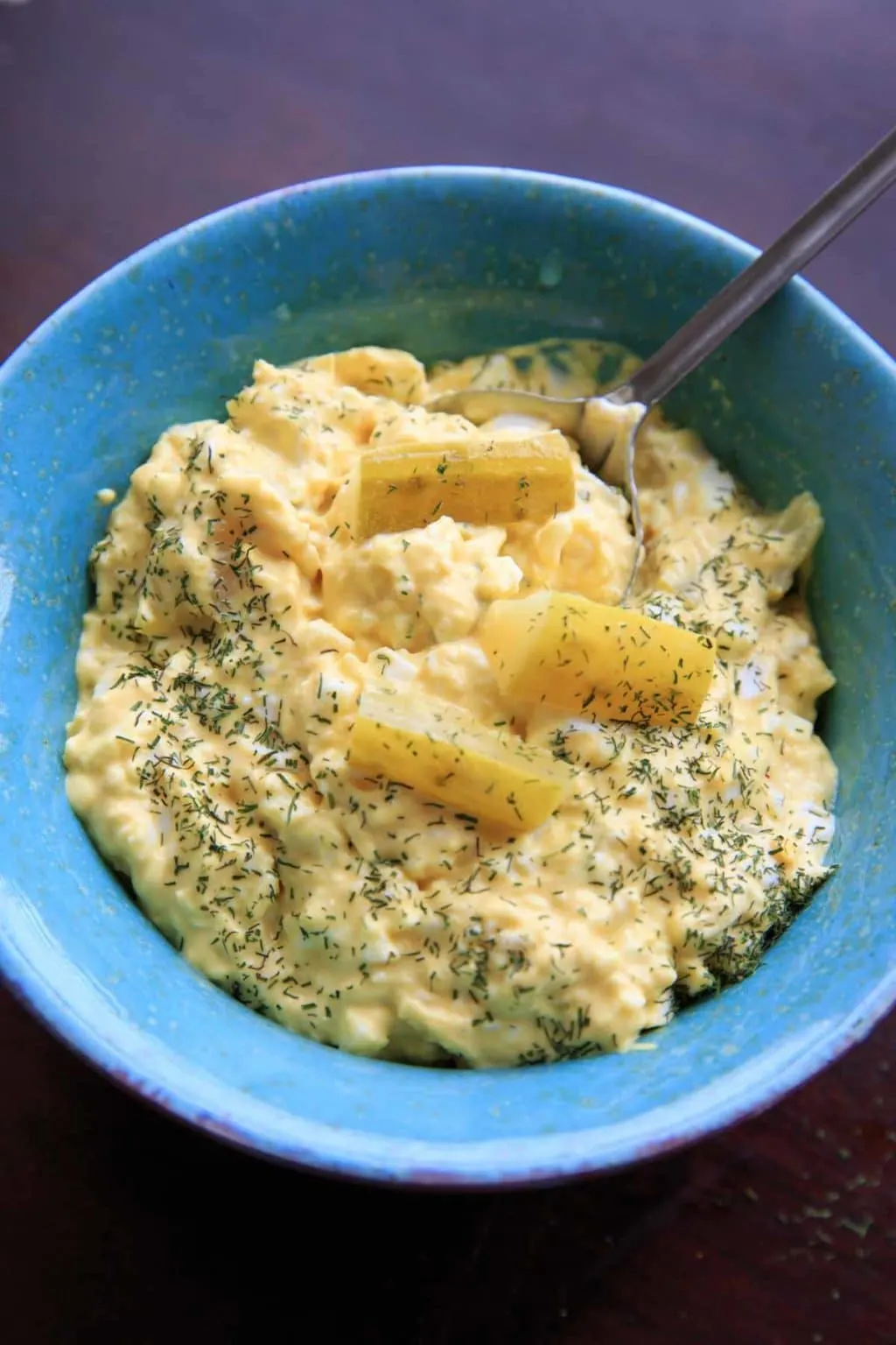 blue bowl of dill pickle egg salad with extra dill sprinkled on top with spoon