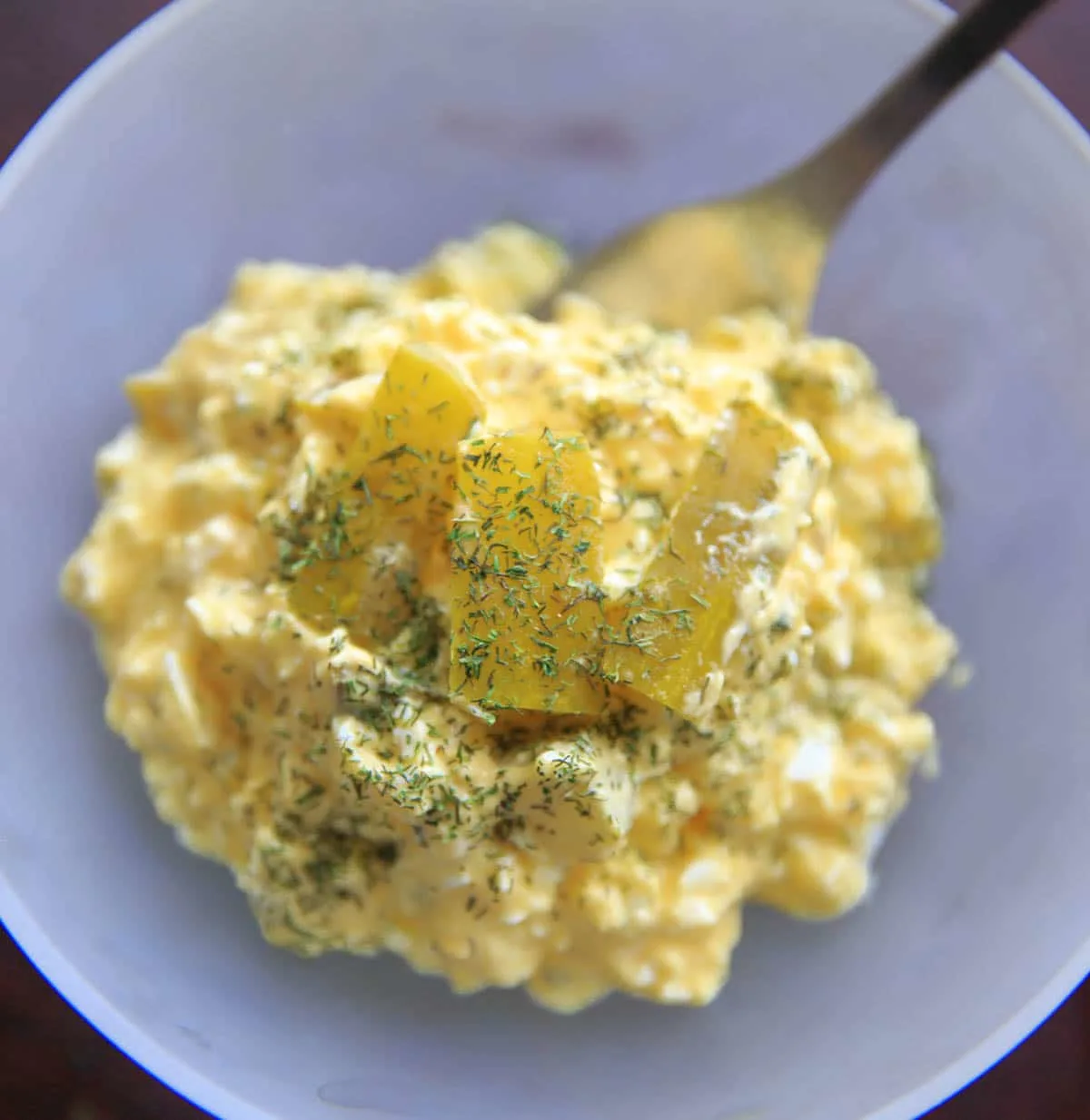 dill pickle egg salad in clear glass bowl with extra pickles on top