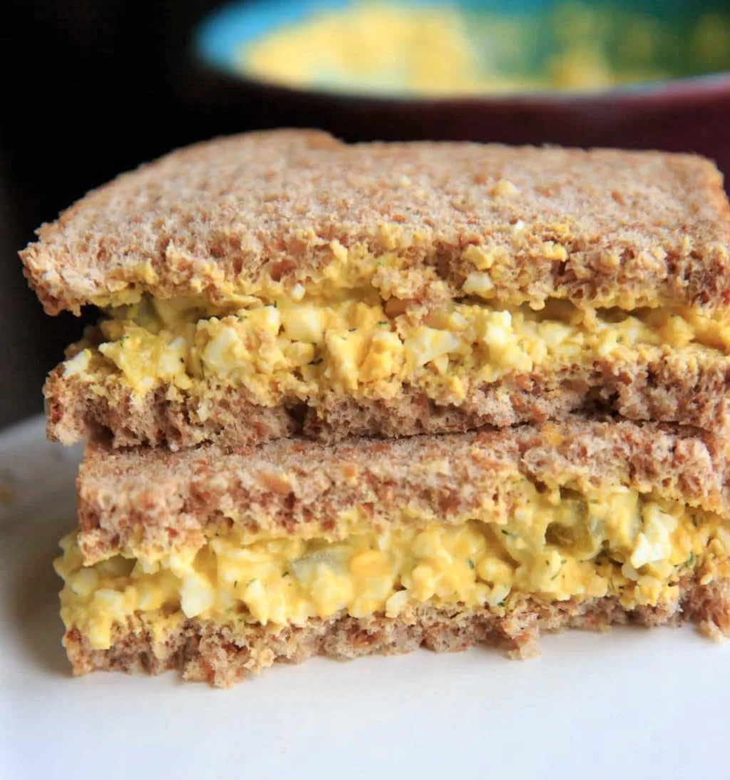 2 sandwich halves stacked on top of each other filled with dill pickle egg salad, on white plate