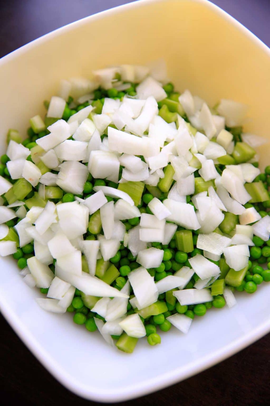 peas, celery and chopped onions in a bowl prepped for pea salad