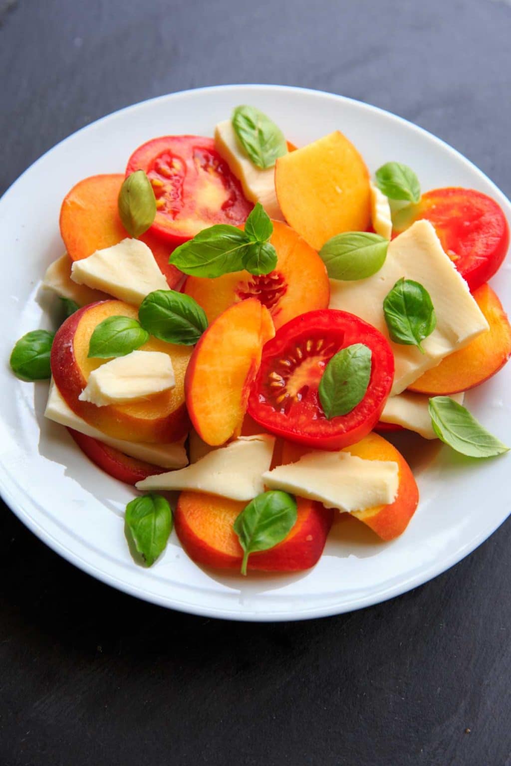 slides peaches and tomato with basil leaves and cheese on white plate