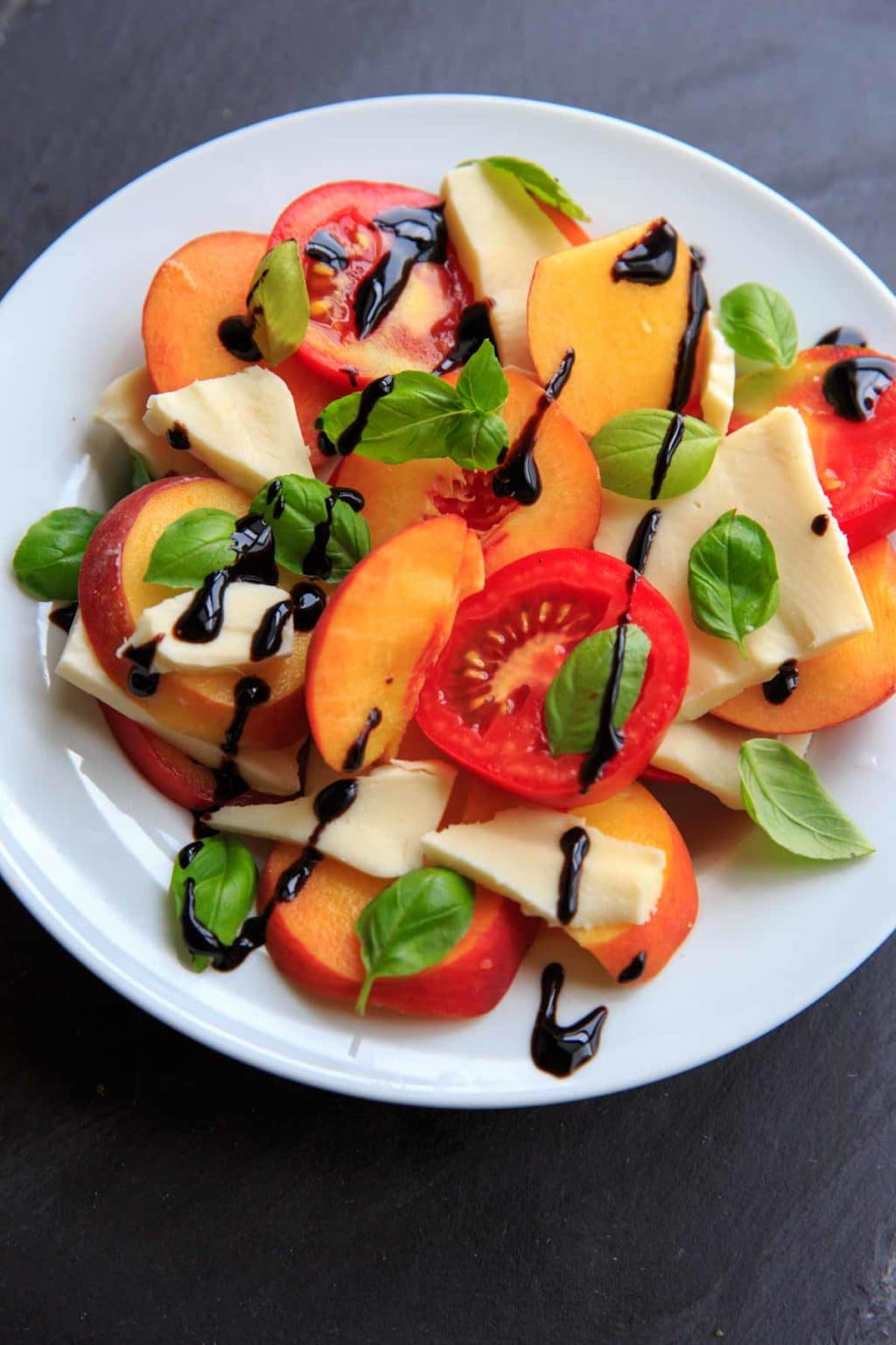 Peach Caprese Salad on white plate with balsamic glaze and basil on top