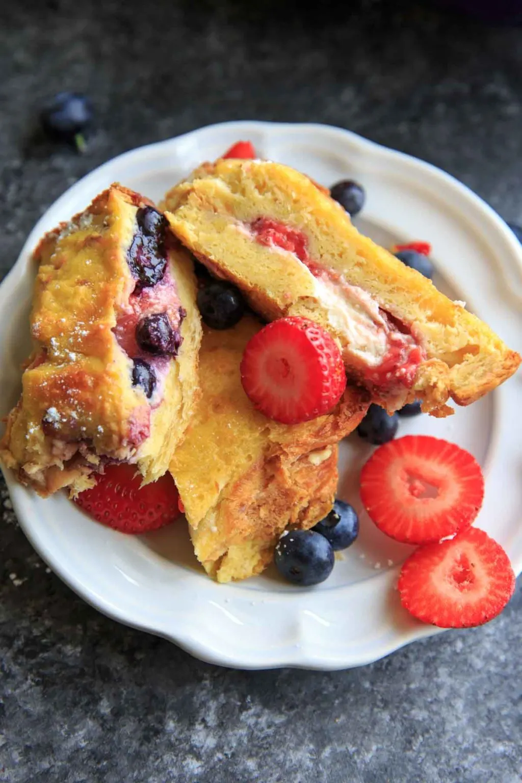 several pieces of stuffed cream cheese french toast with berries piled on white plate