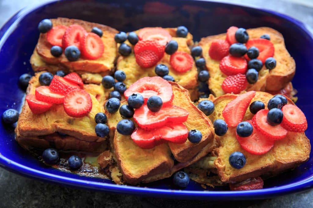 stuffed french toast topped with berries in blue casserole pan