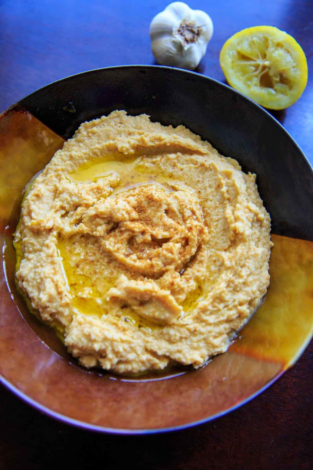 Lemon Garlic Hummus in bowl with squeezed lemon and garlic bulb in background