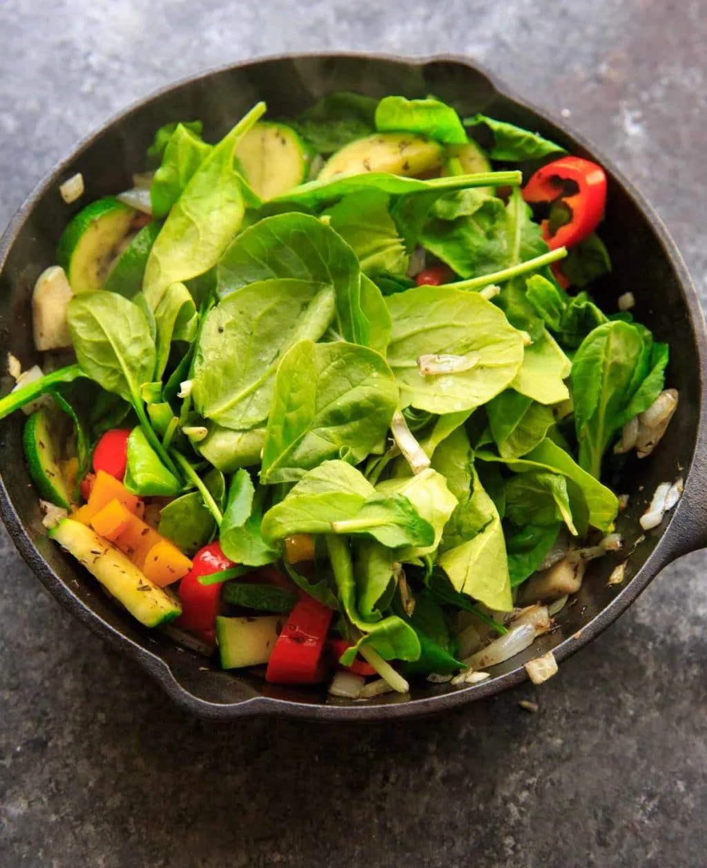 Adding spinach to sauteed vegetables with zucchini, onion, mini sweet peppers