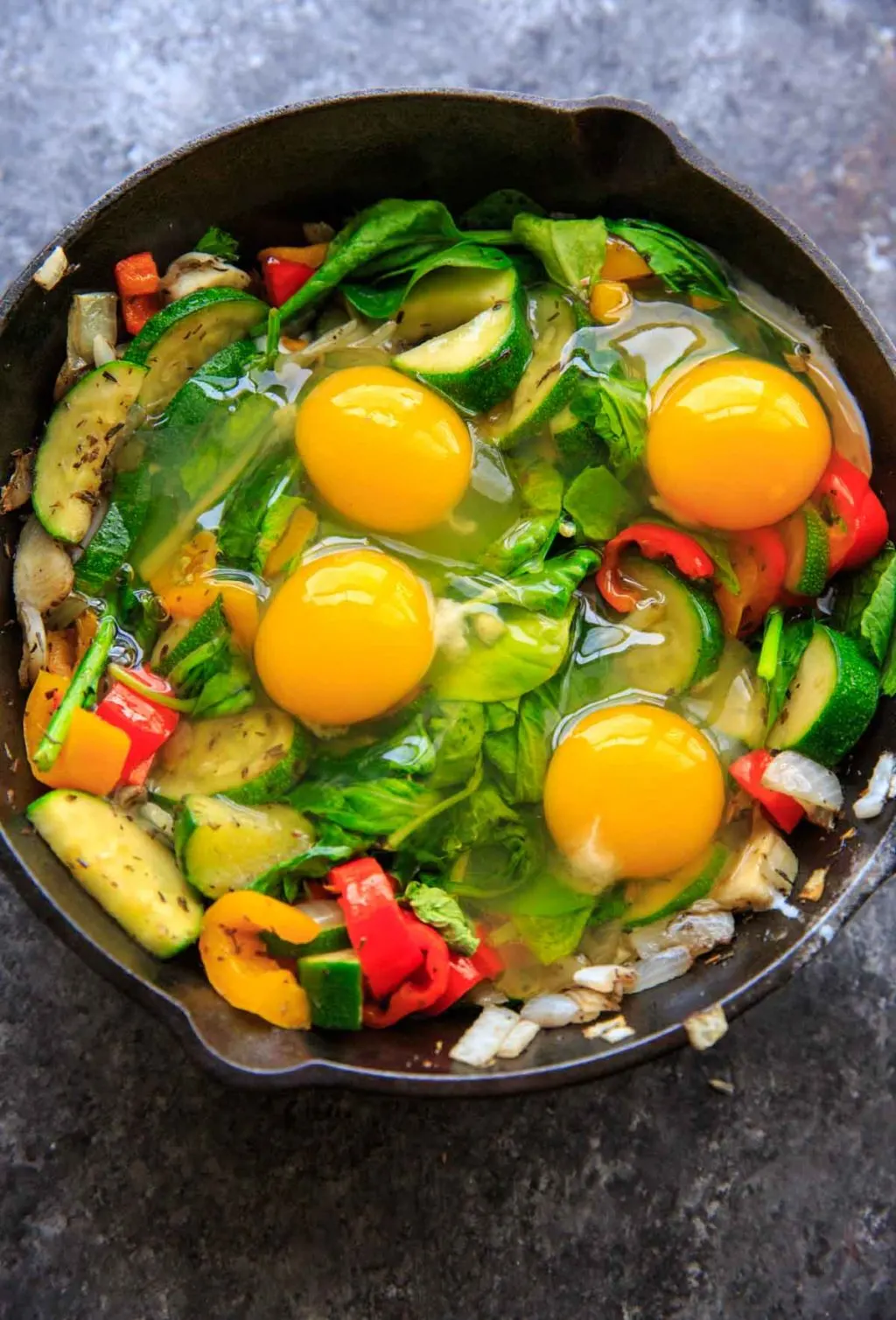 Adding eggs to sauteed vegetables with zucchini, onion, mini sweet peppers and spinach