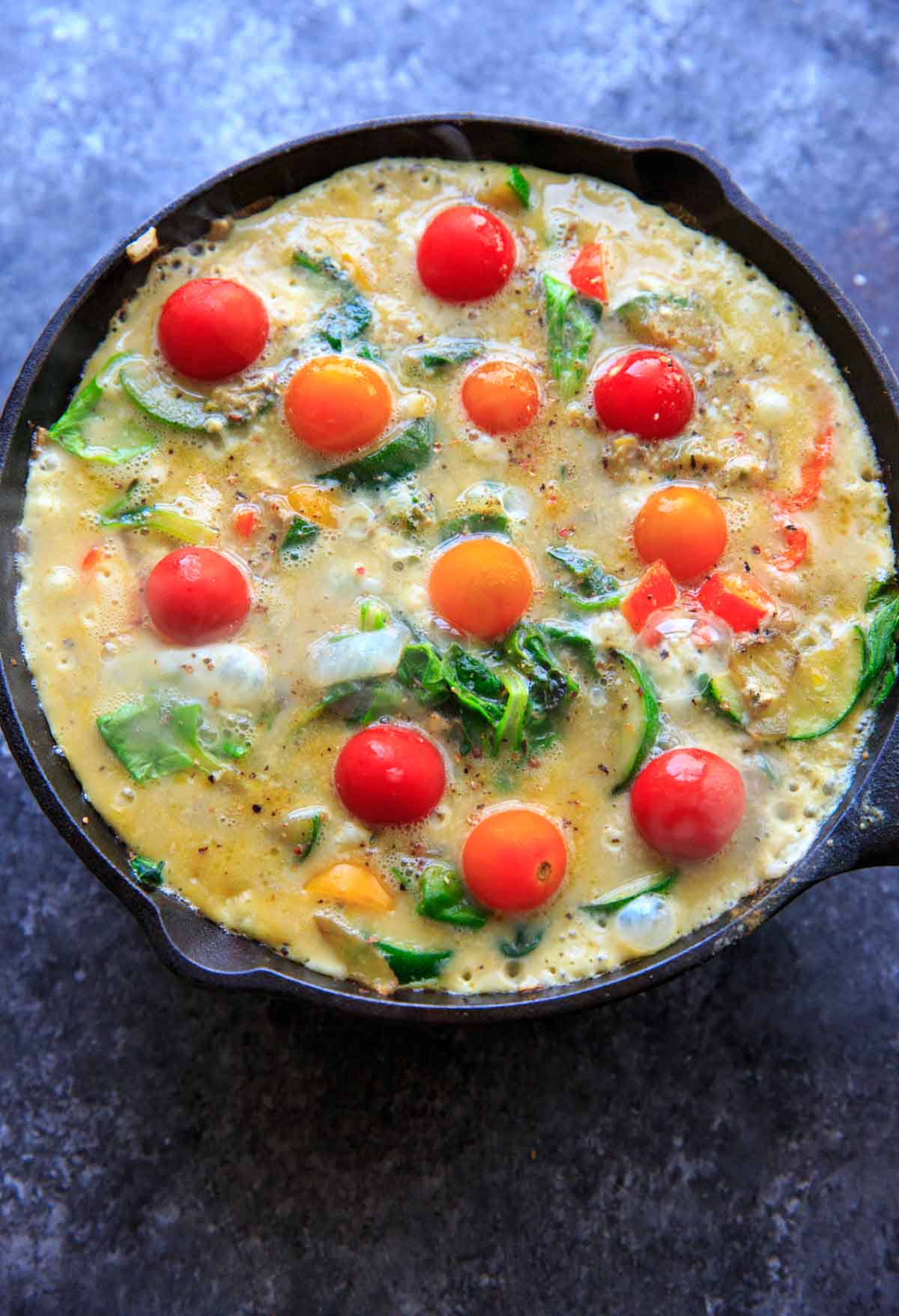 Mixing the eggs with sauteed vegetables with zucchini, onion, mini sweet peppers and spinach. Topped with mini heirloom tomatoes.