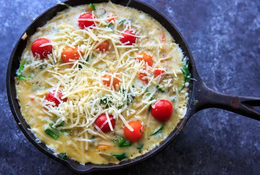 Mixing the eggs with sauteed vegetables with zucchini, onion, mini sweet peppers and spinach. Topped with mini heirloom tomatoes and cheese.