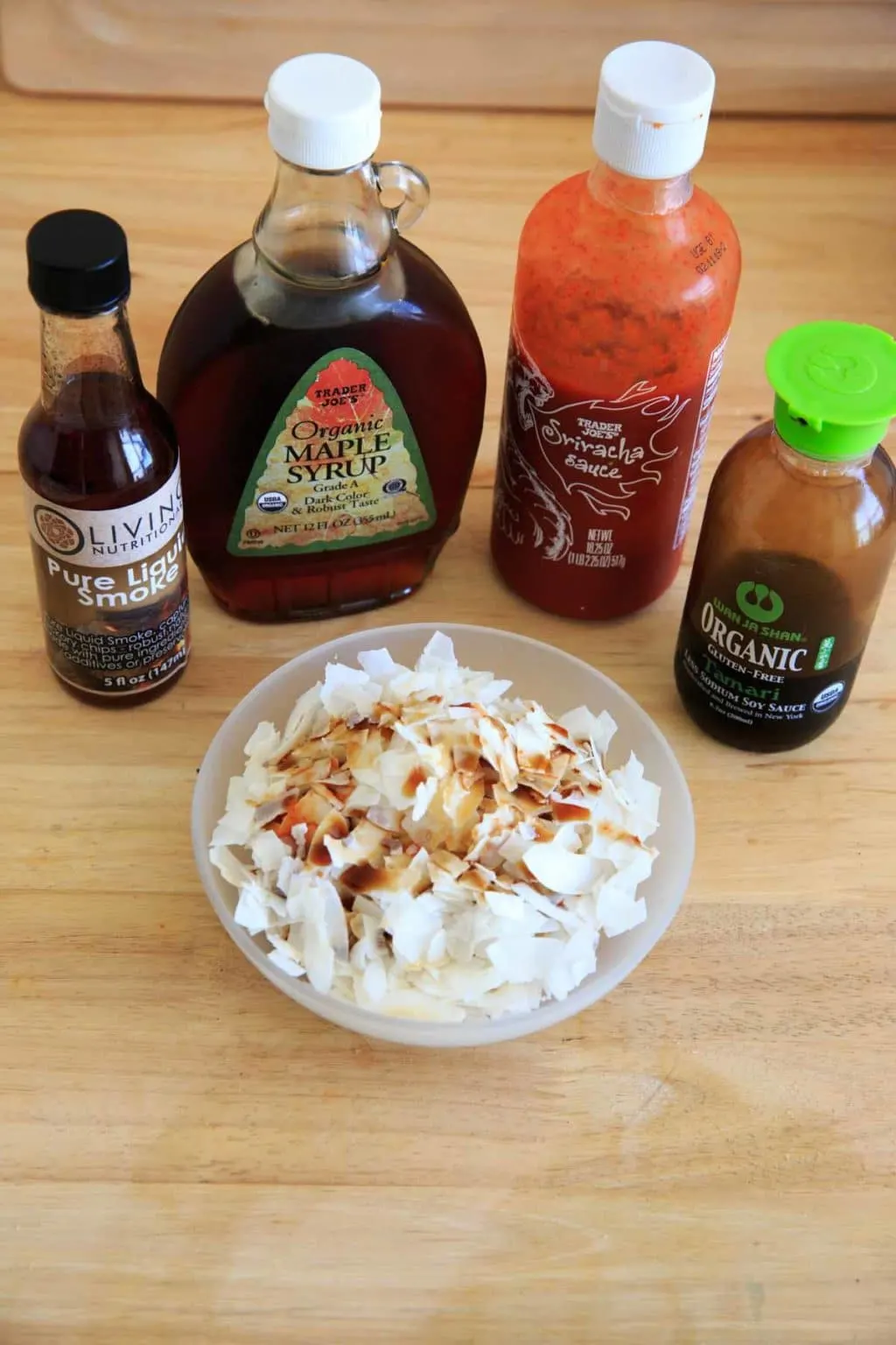 all ingredients to make vegan coconut bacon - coconut flakes, liquid smoke, maple syrup, sriracha sauce, tamari sauce