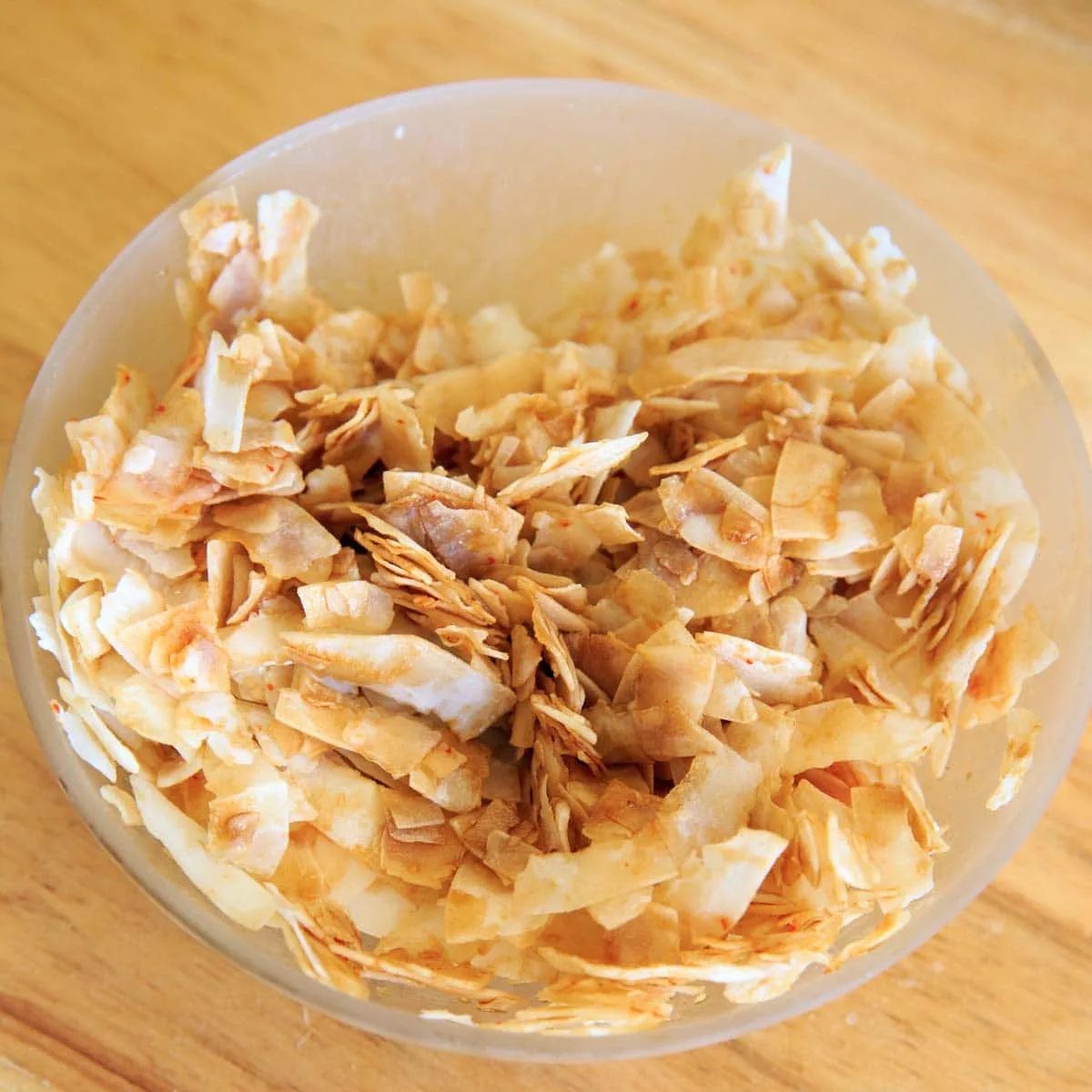 coconut chips in clear bowl with some of the liquid added to make bacon (before mixing)