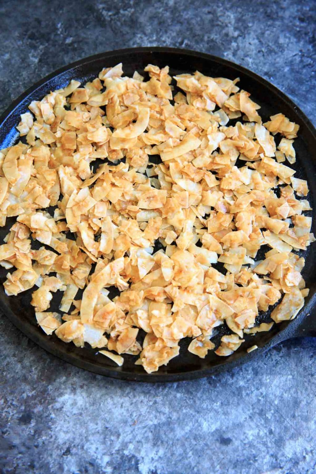 Coconut Chips spread out on cast iron pan before baking into vegan bacon