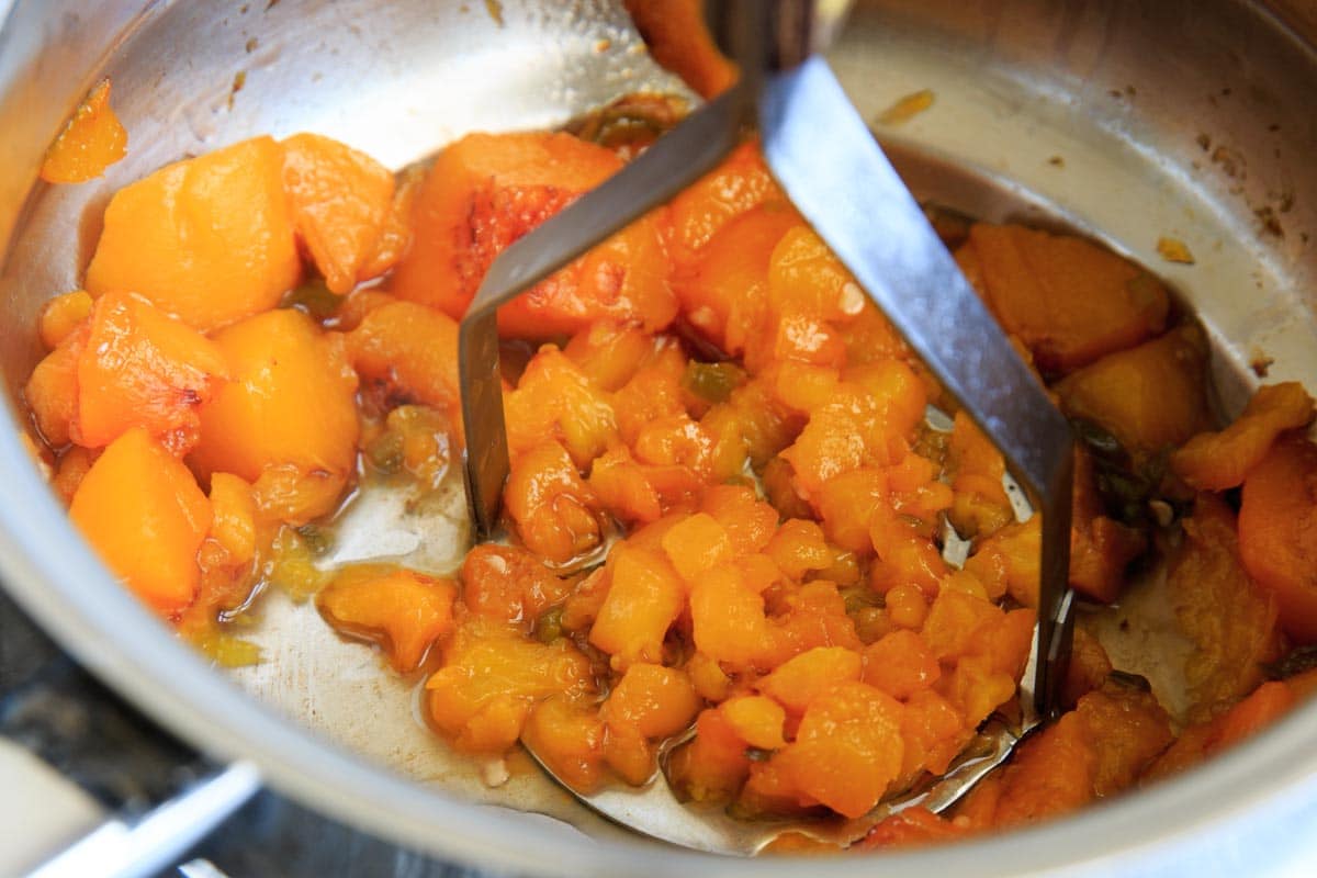 mashing the cooked peaches and jalapeno