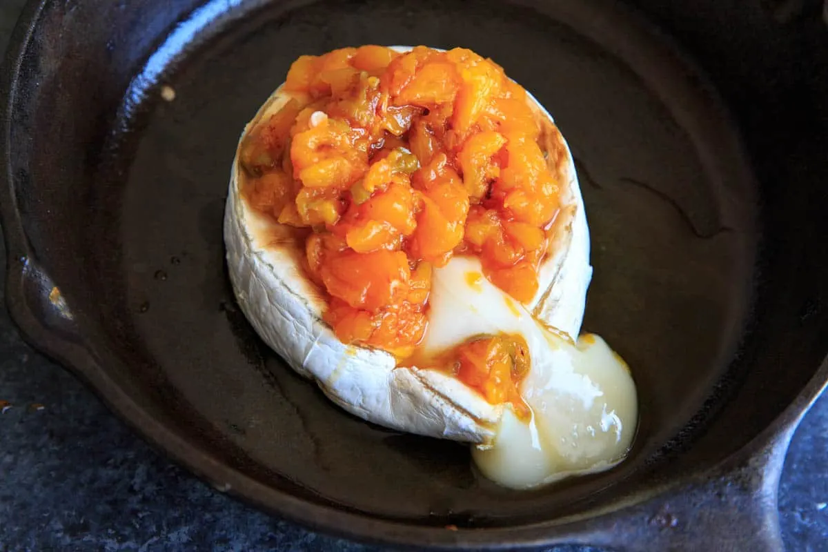 baked brie topped with peaches and cheese cut and oozing into pan