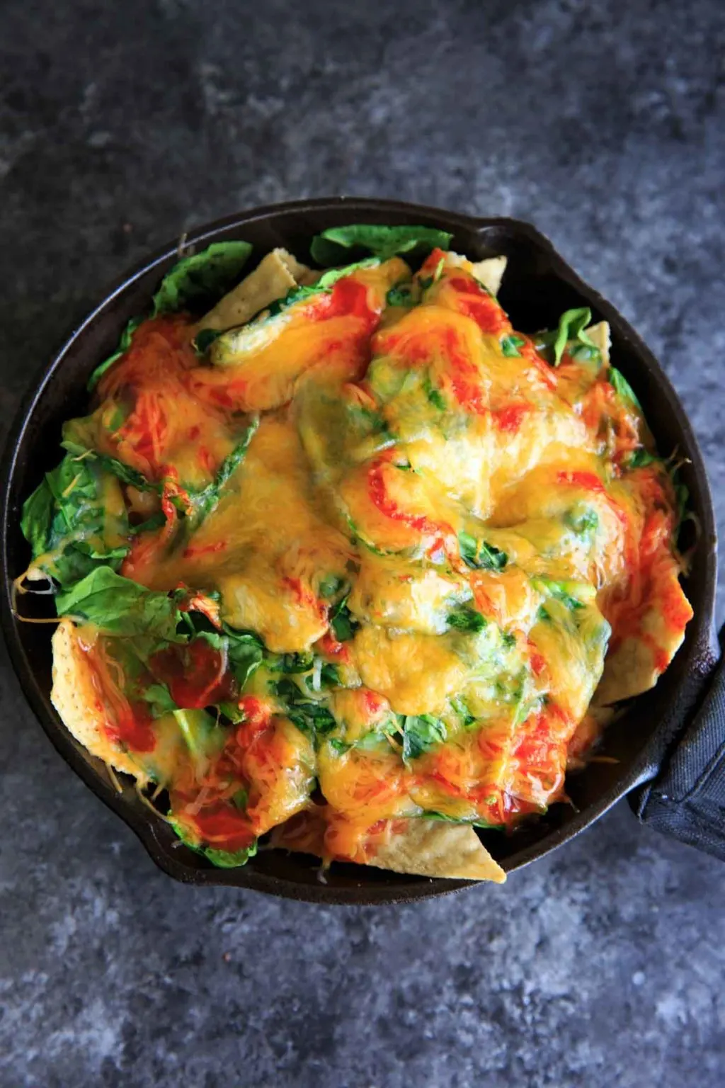 Oven-baked spinach nachos in a cast iron skillet. A great party snack, meal for 2 (or 1!) that has a little extra nutrition with greens.