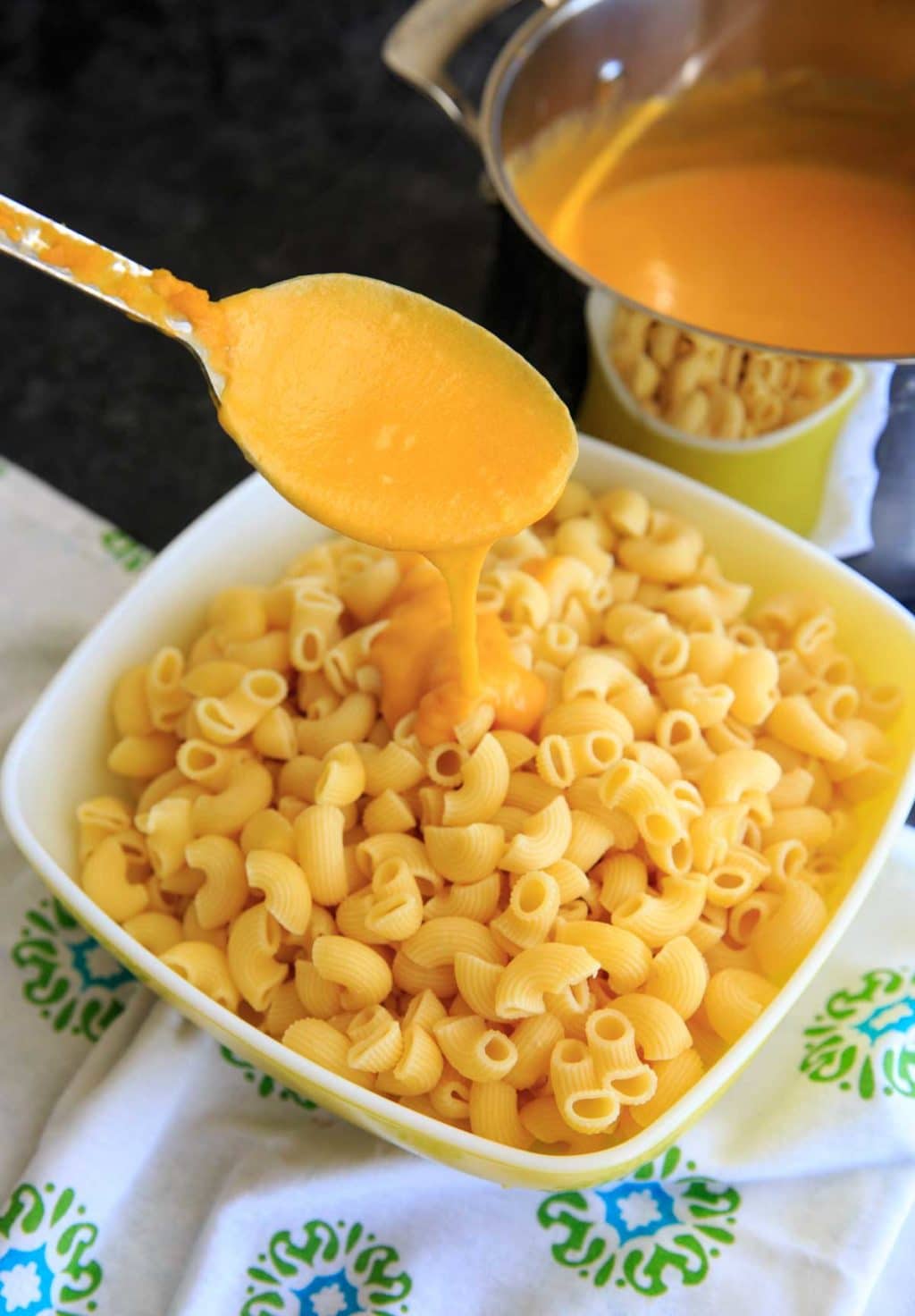 spooning the butternut squash and sharp cheddar cheese sauce over a big bowl of macaroni