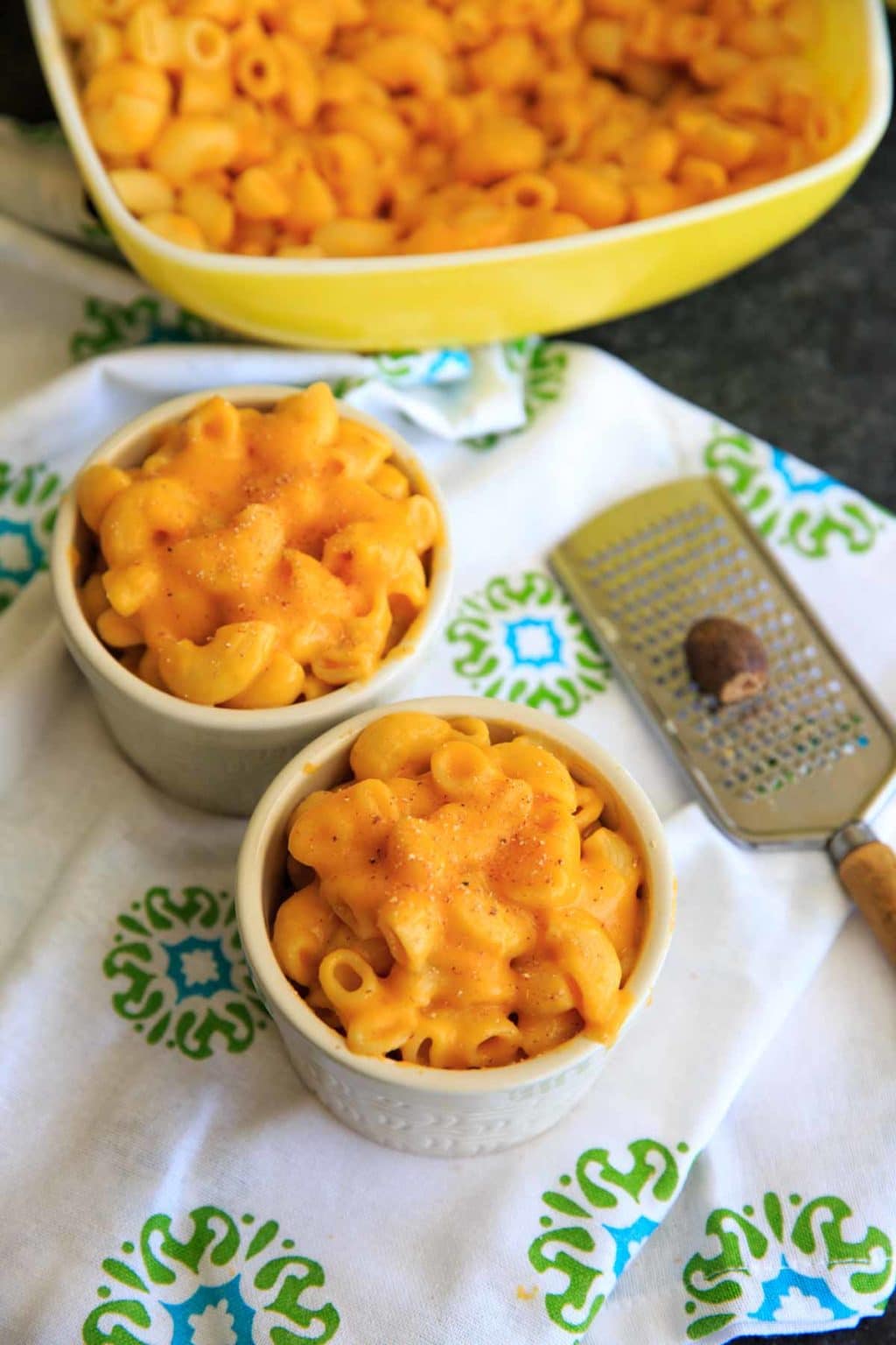 two mini baked bowls of butternut squash macaroni and cheese with grater and nutmeg to the side