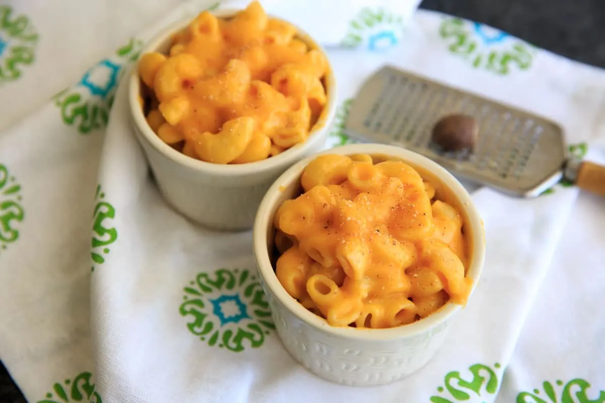 two mini baked bowls of butternut squash macaroni and cheese with grater and nutmeg in background