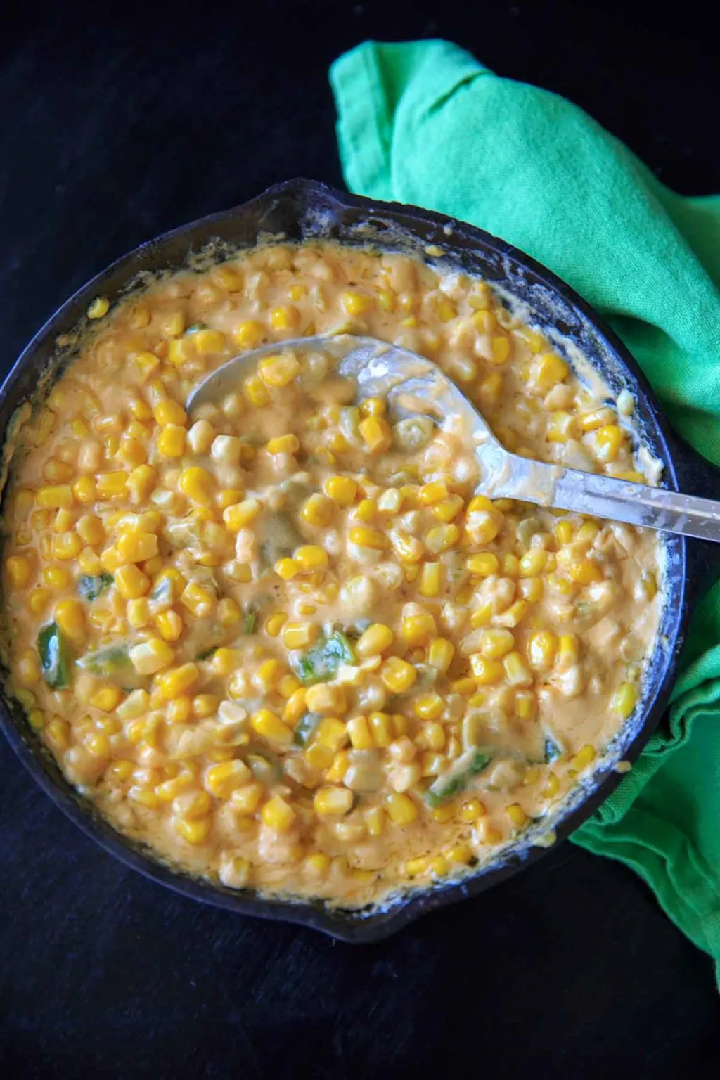 Creamy Spicy Hot Corn Dip in cast iron skillet with serving spoon and green napkin