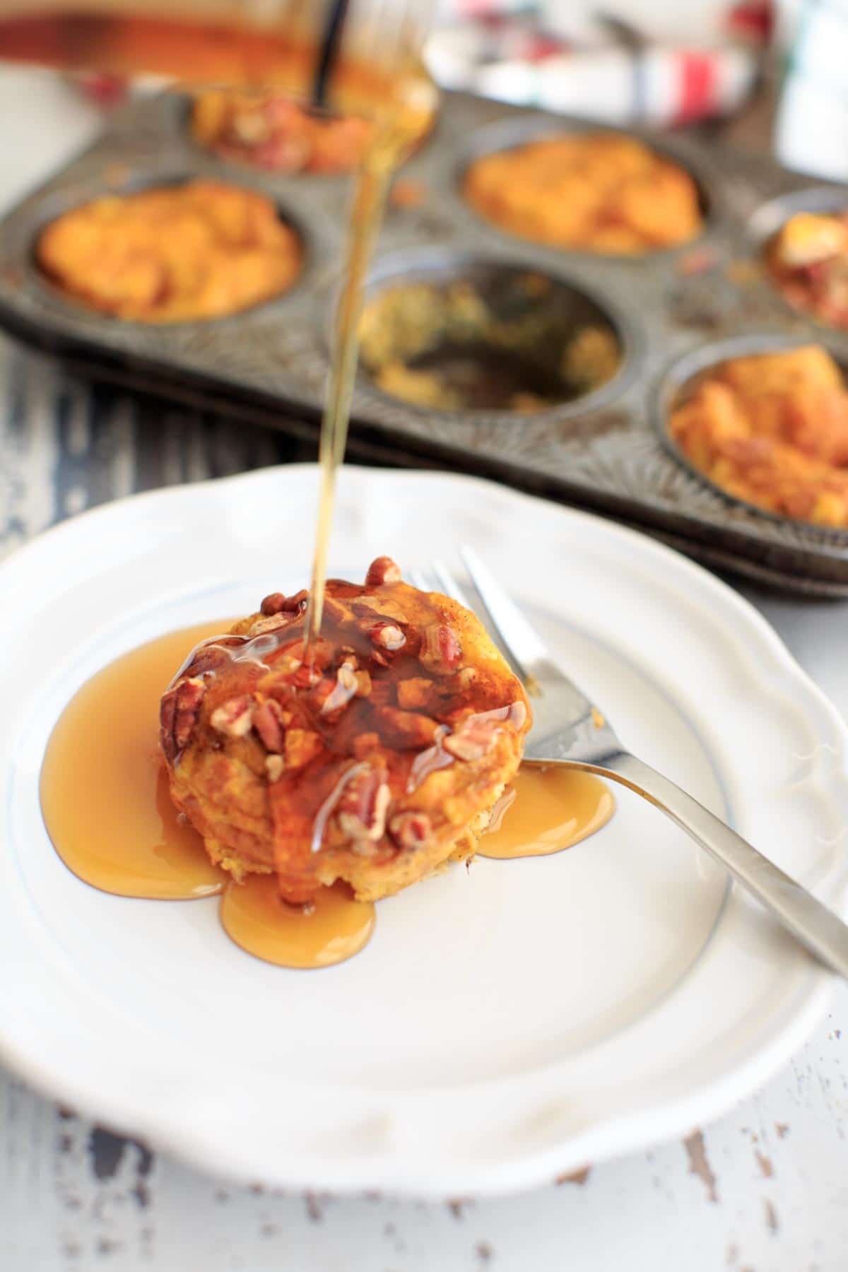 Pumpkin French Toast Muffin Cup on white plate, pouring syrup on top