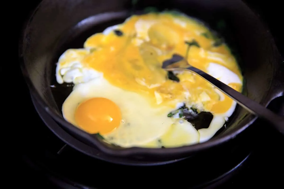 Two eggs cooking on the stove for a breakfast pita wrap: one scrambled, one sunny side up