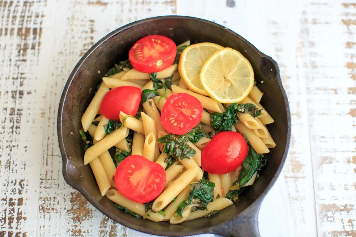 Lemon Spinach Pasta with lemon slices and tomatoes in a cast iron pan - landscape