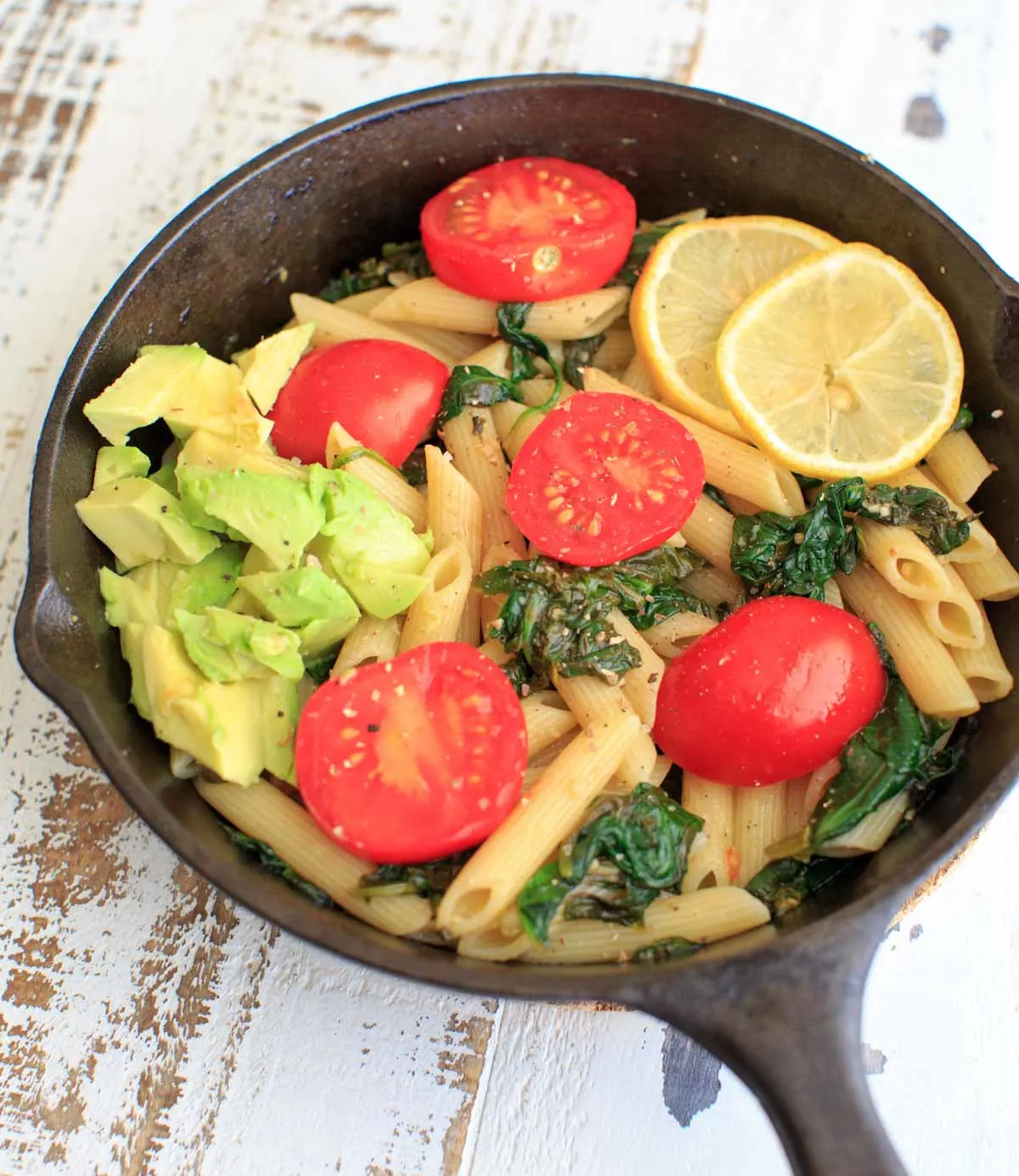 Lemon Spinach Pasta with lemon slices, tomatoes and avocado in a cast iron pan