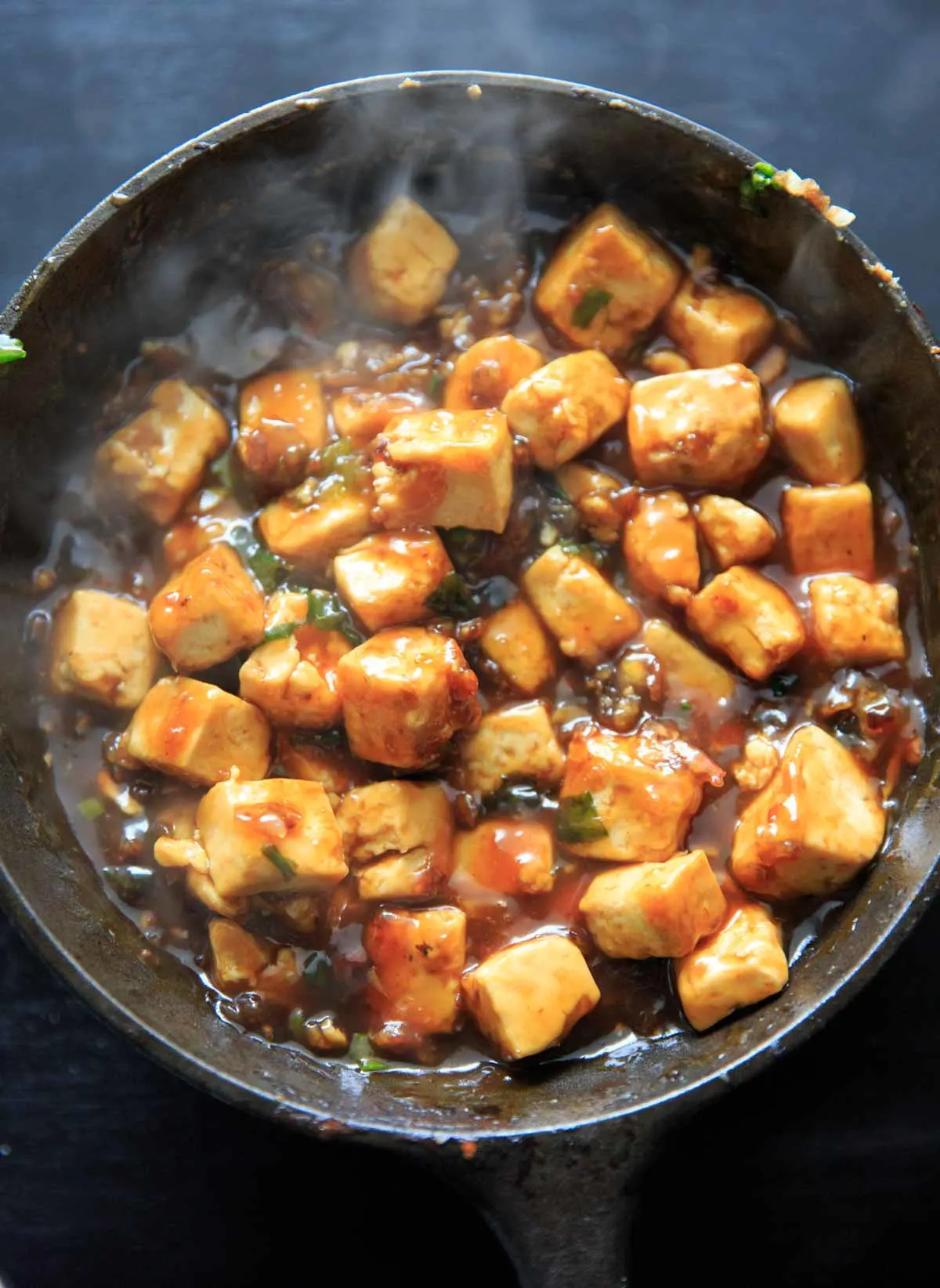General Tso's Tofu cooking in sauce in a cast iron pan.