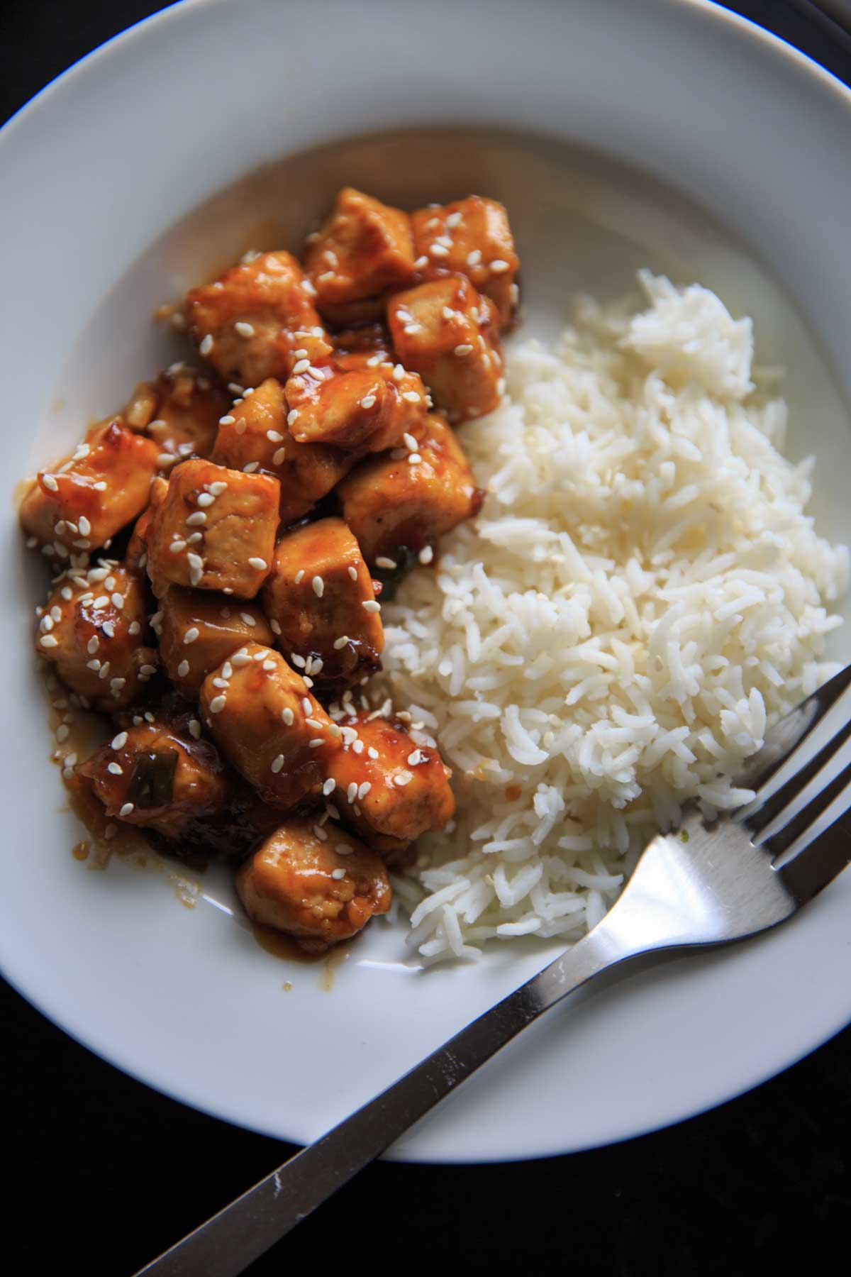 General Tso's Tofu serve with rice in white bowl with fork