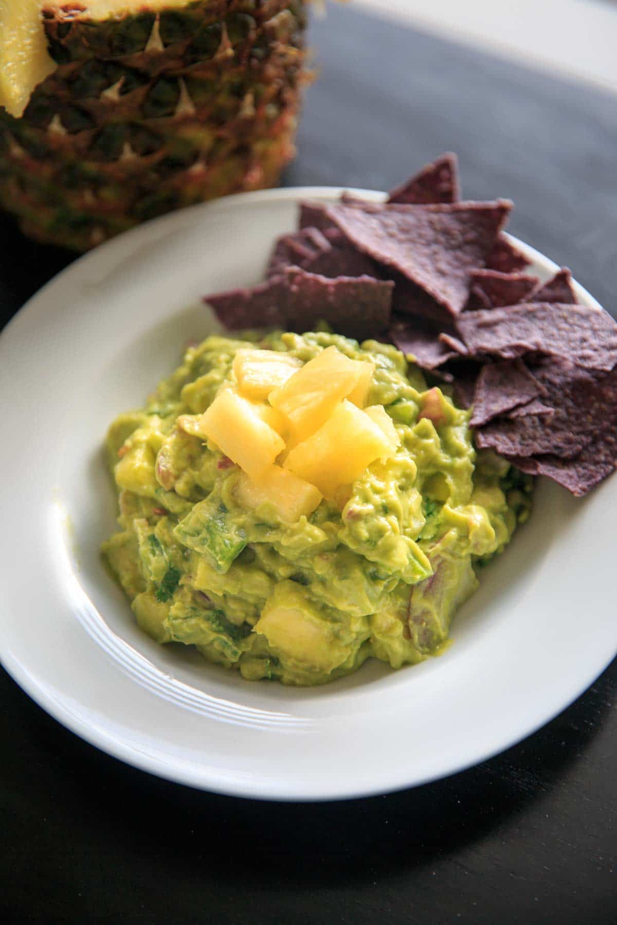 tropical guacamole topped with extra chunks of pineapple on white bowl with pineapple in background