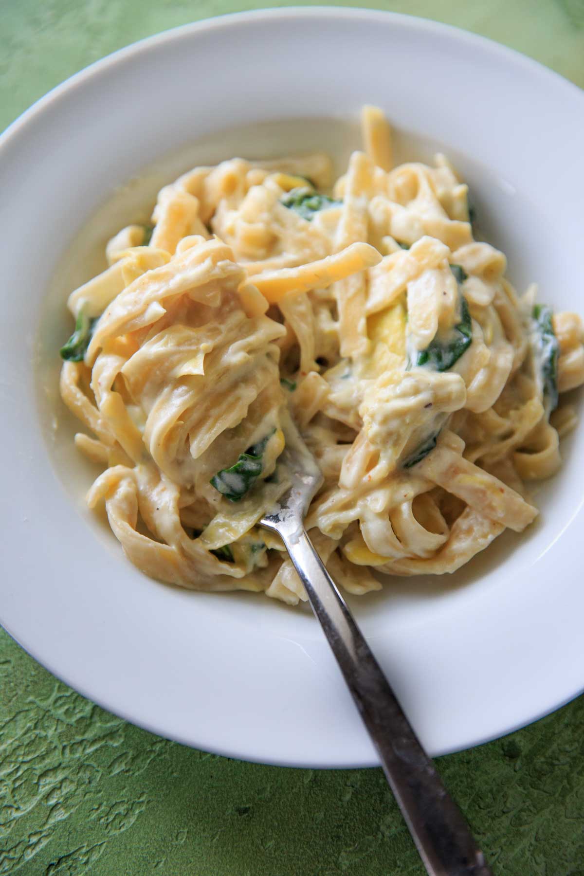 white plate with cooked spinach and artichoke pasta