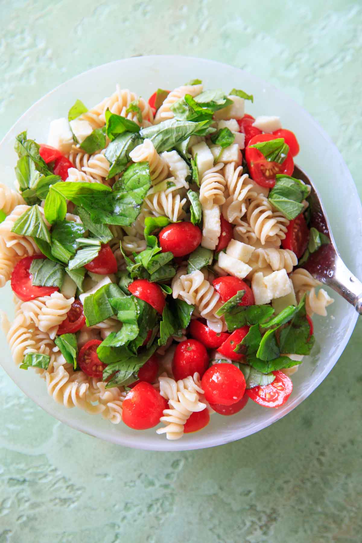 mixing tomatoes, basil, mozzarella, olive oil and pasta in bowl