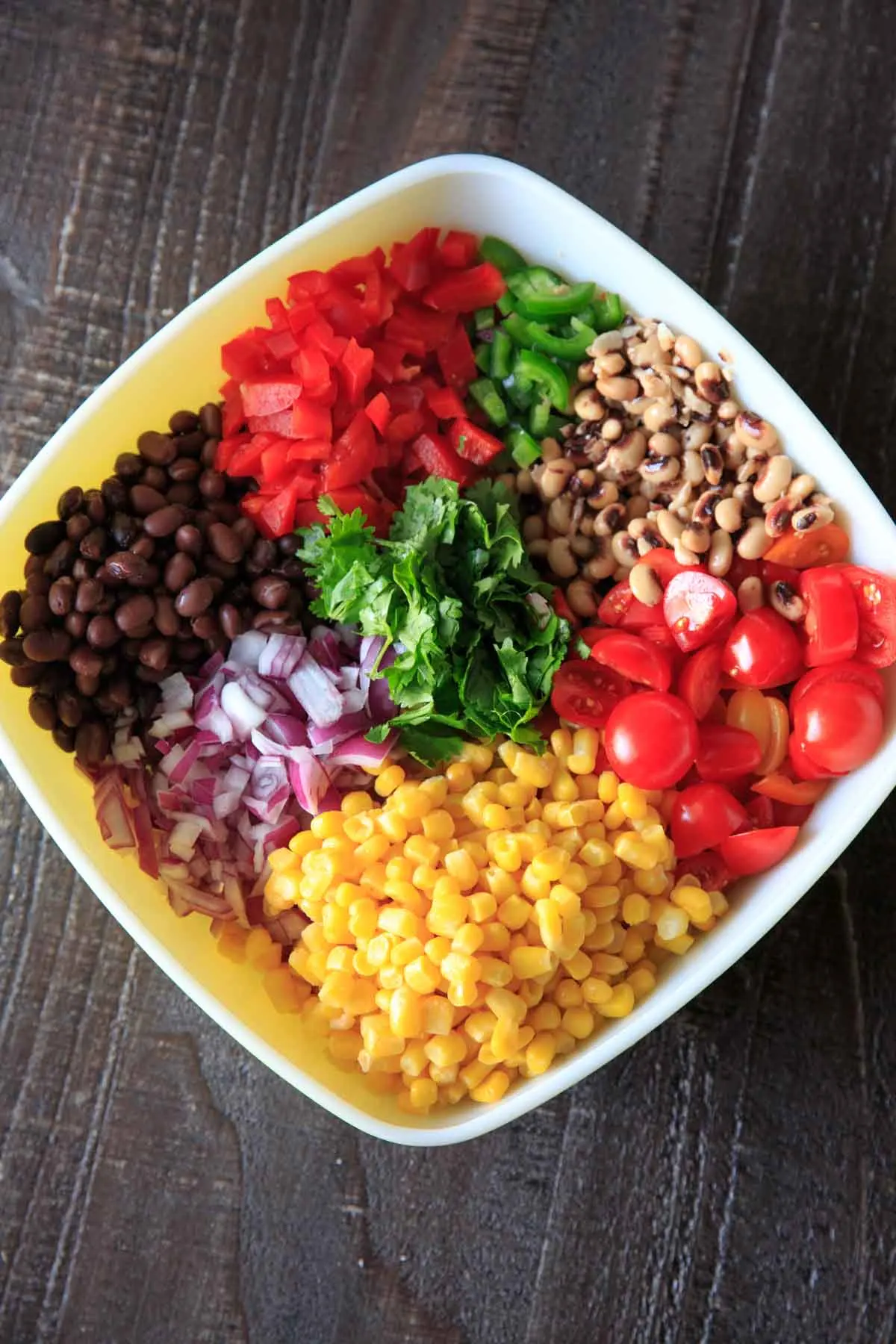 Assembling cowboy caviar with black eyed peas, black beans, onion, tomato, corn, cilantro and bell pepper
