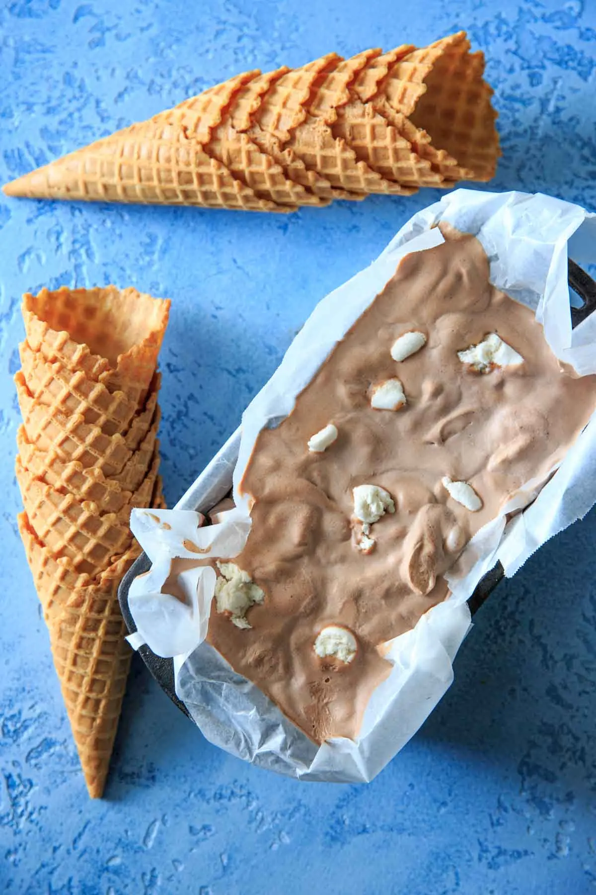 Hot chocolate ice cream frozen with stacked ice cream cones laying next to it