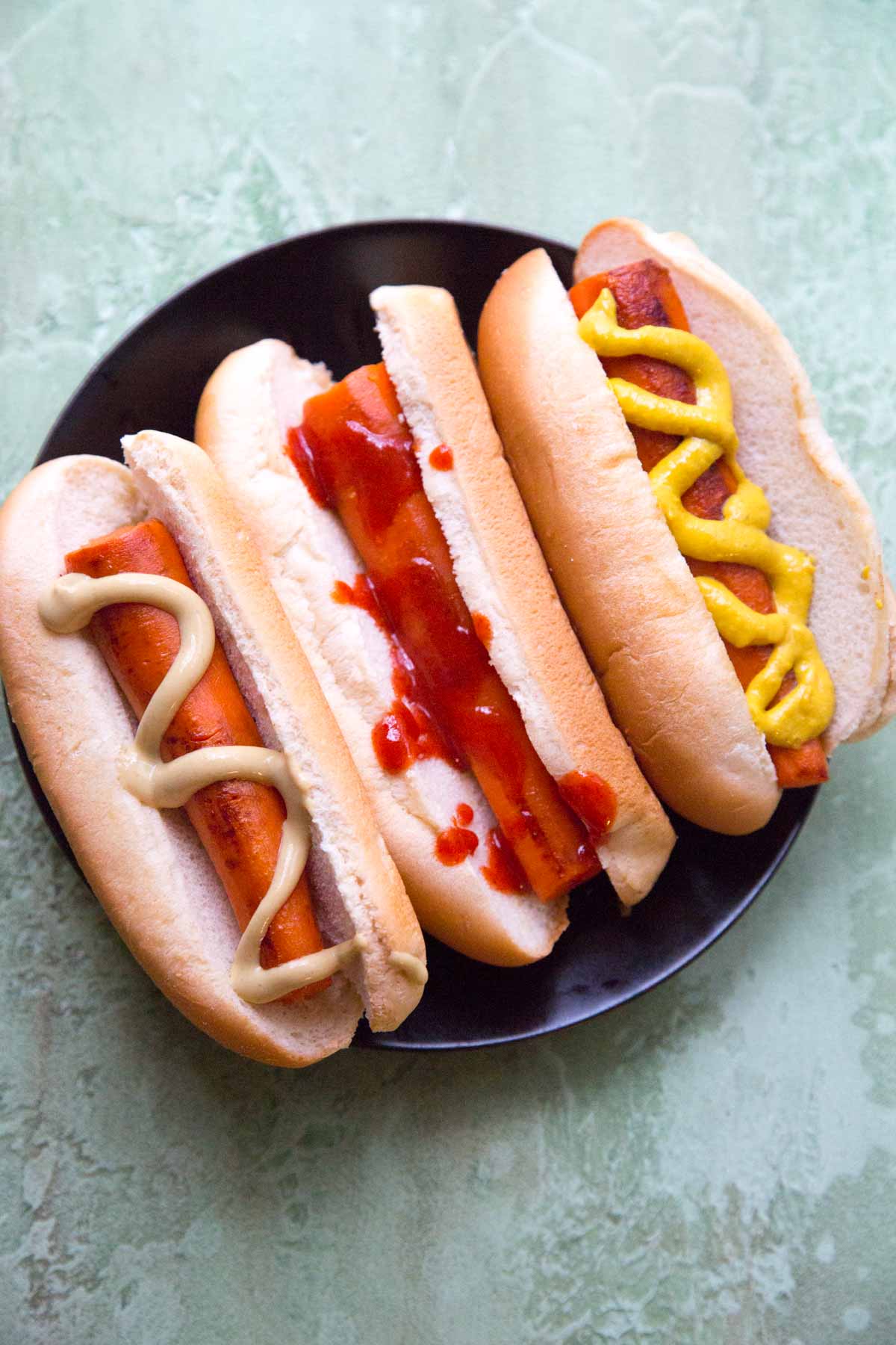 3 carrot not dogs in a bun on black plate with toppings