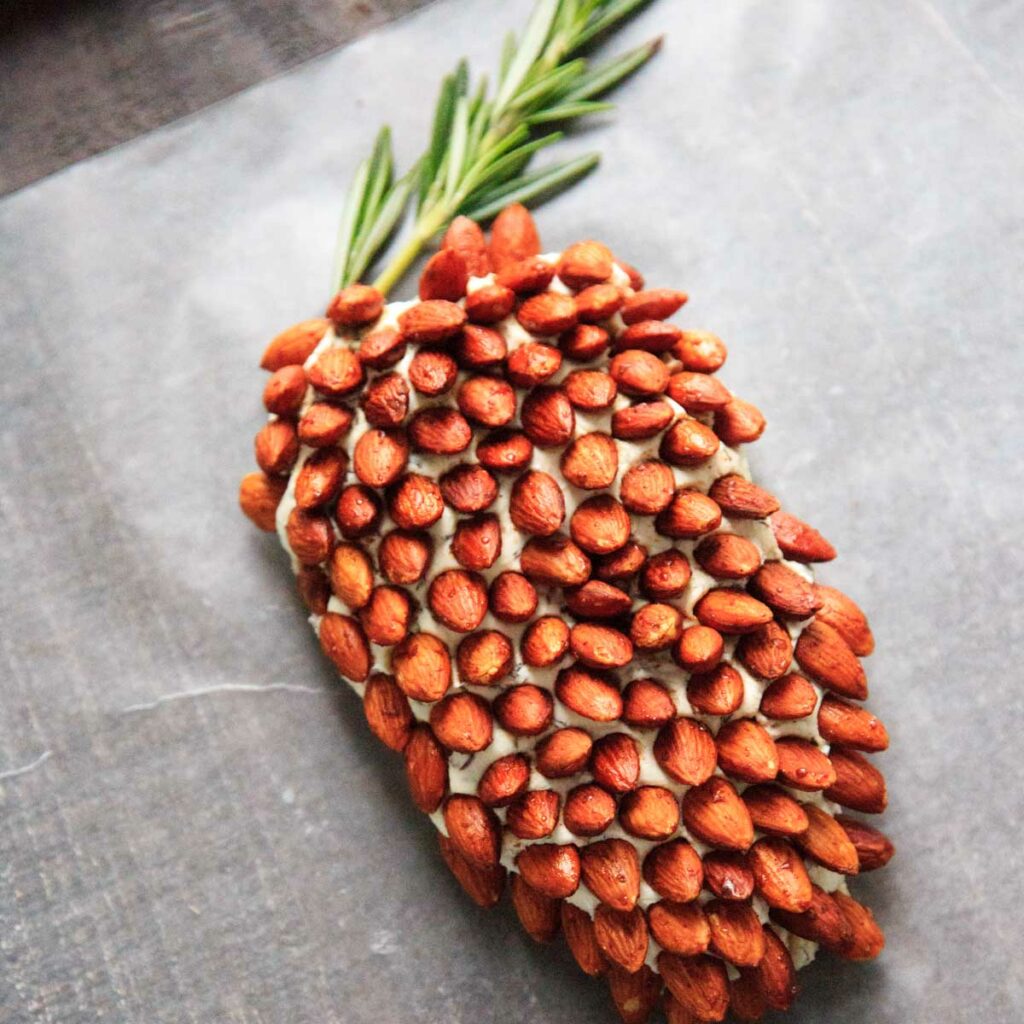 A cheese ball that looks like a pine cone! This will be a hit at your party. Using rosemary sprigs and cinnamon honey roasted almonds.