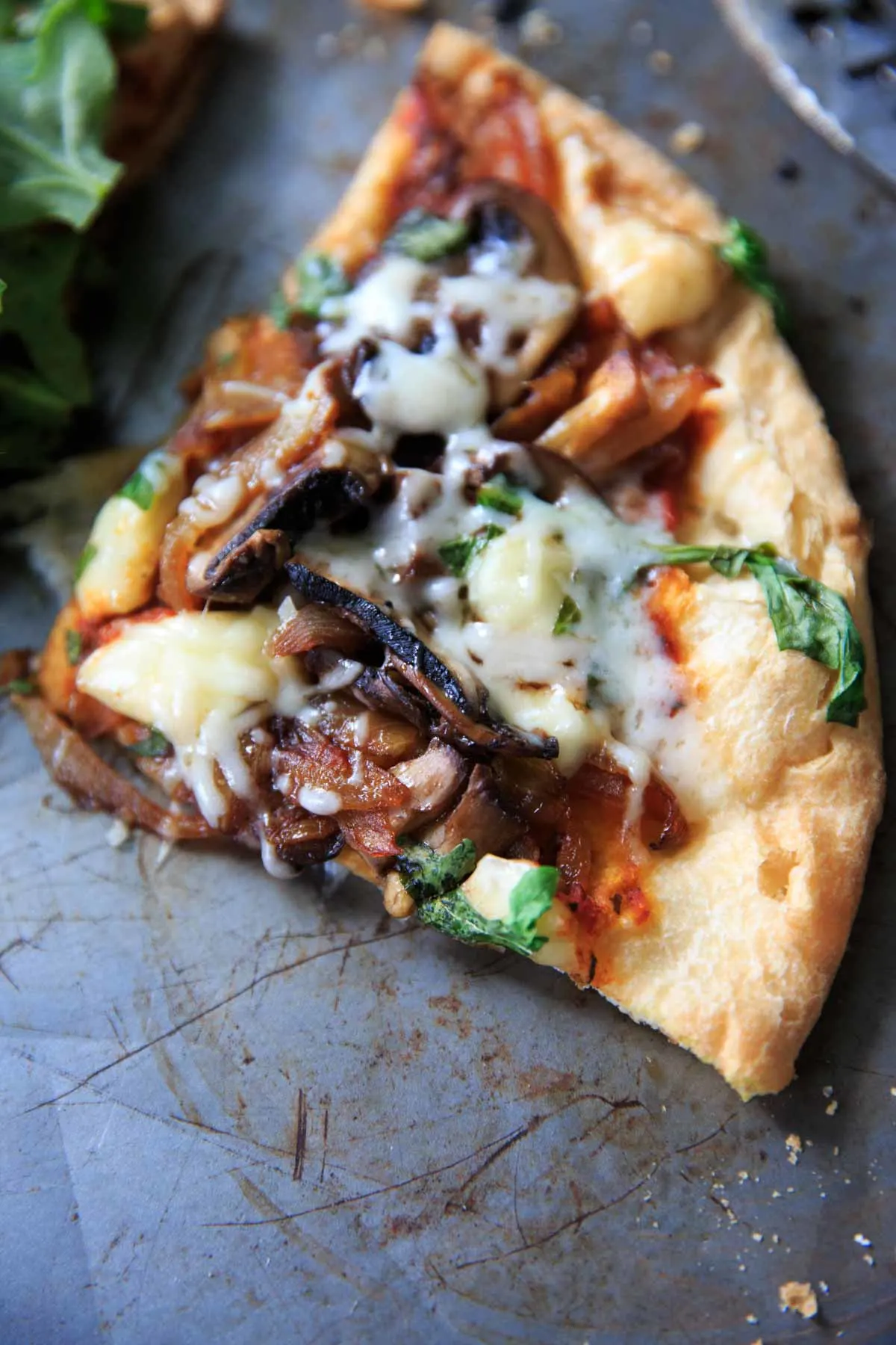 Close up of a pizza slice with caramelized onions, mushrooms and brie cheese before topping with arugula