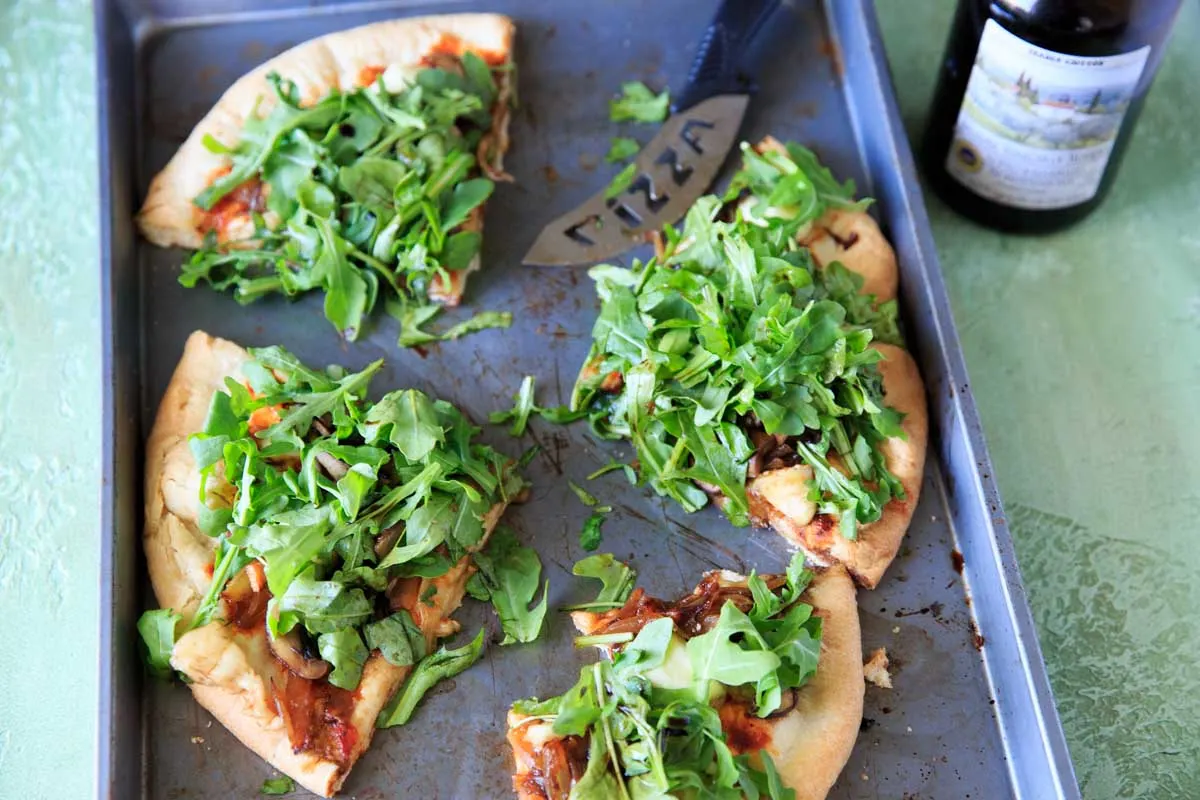 Homemade pizza with caramelized onions, fresh baby arugula and brie cheese, sliced into four pieces on baking sheet