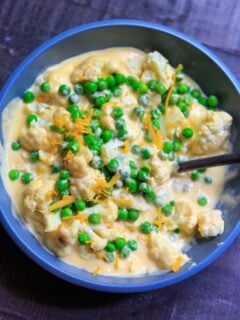 cheesy cauliflower florets with peas in bowl and shredded cheese on top