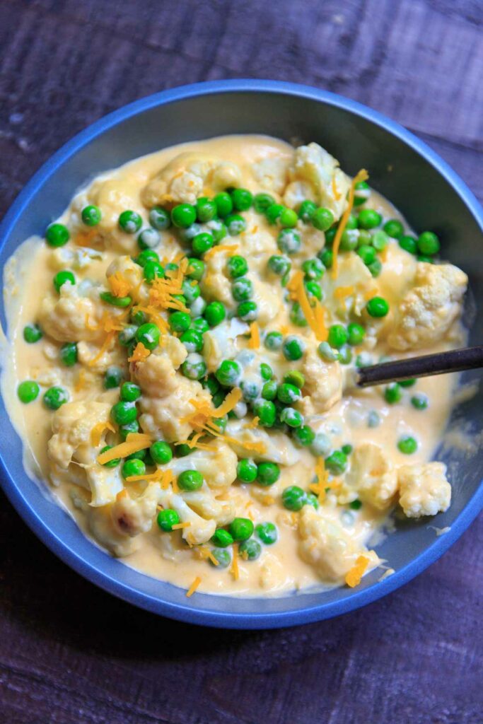 cheesy cauliflower florets with peas in bowl and shredded cheese on top