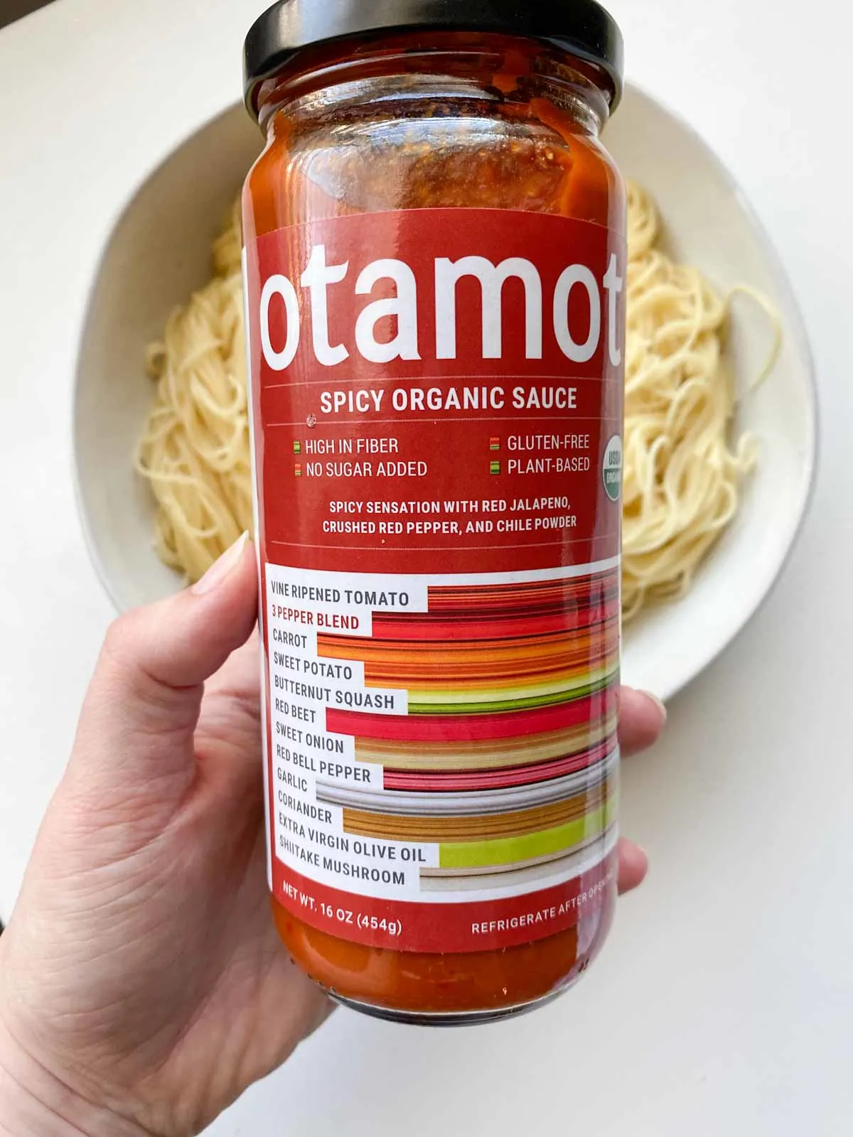 jar of Otamot spicy organic sauce over a bowl of spaghetti noodles