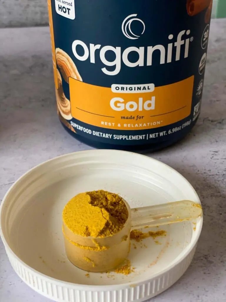 organifi gold juice powder in tub with a scoop out shown on lid