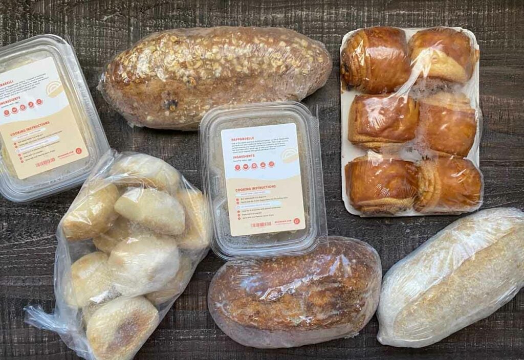 contents of wildgrain monhtly box - 3 loaves of sourdough breads, two boxes of pasta, bag of sourdough rolls and 6 chocolate croissants