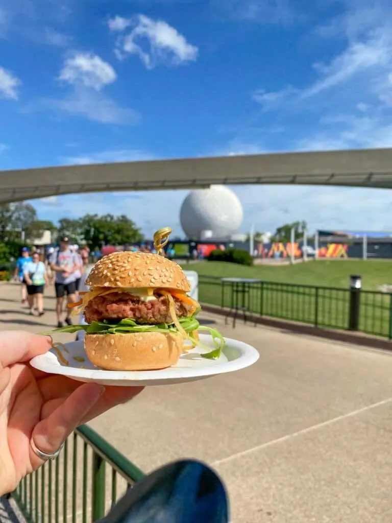 Earth Eats impossible burger slider held up against the Epcot globe