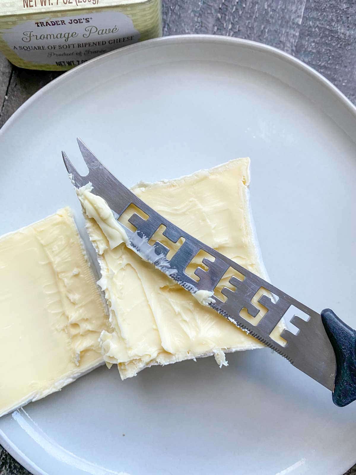 Fromage pavé cheese block from Trader Joe's sliced in half with knife that says "cheese"
